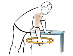 Un hombre inclinado hacia delante con una mano sobre la mesa para apoyarse balancea el otro brazo en círculos para hacer un ejercicio de hombros.
